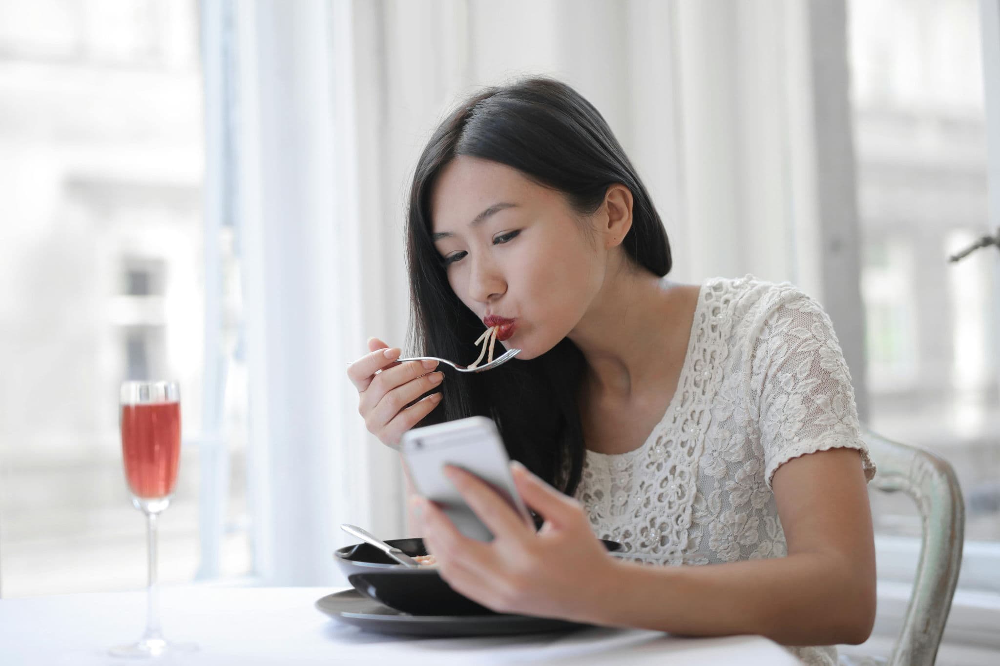 亞洲女子在咖啡廳邊吃麵邊使用手機,準備留下 Google 評論